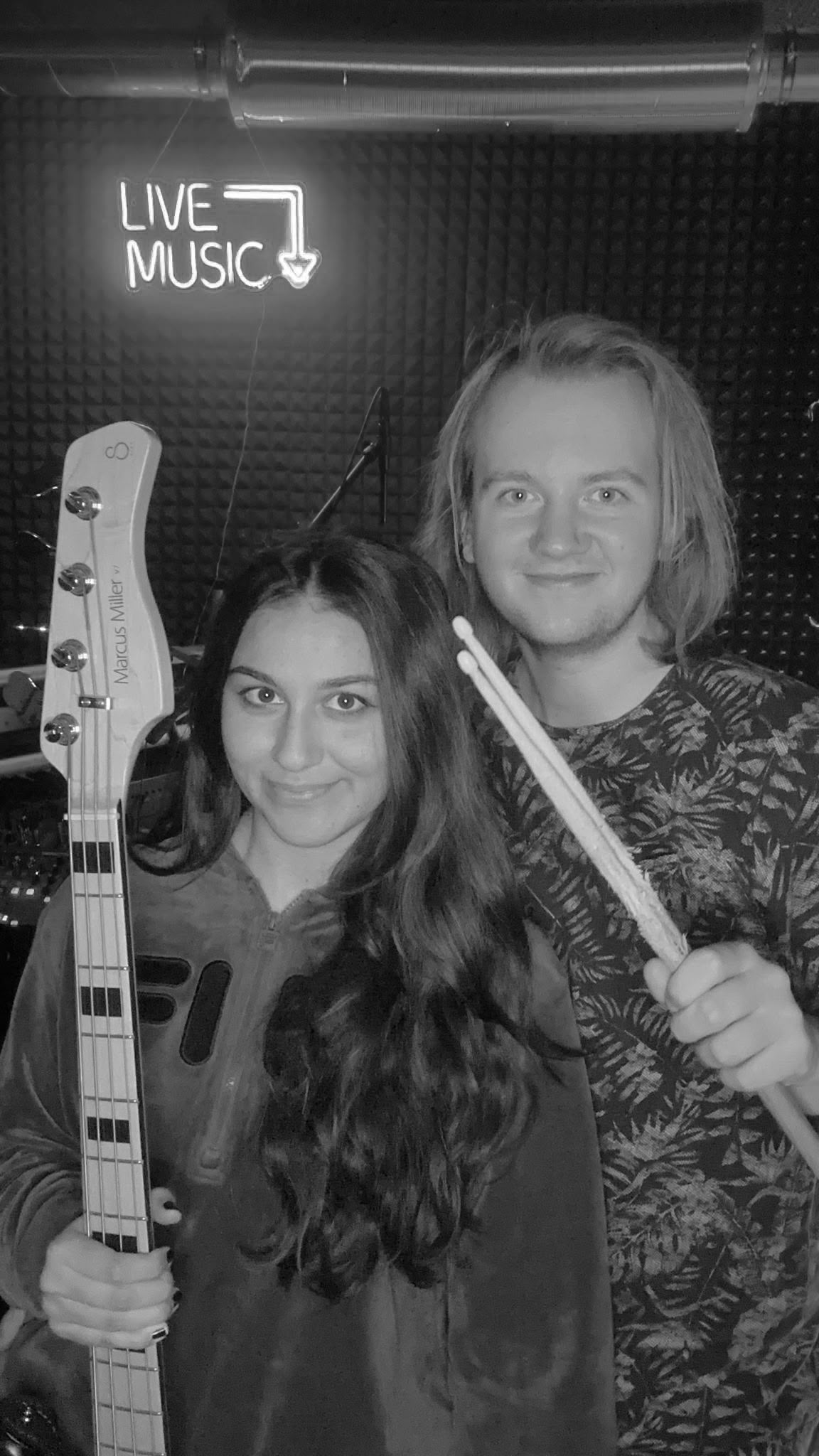 Groovve – Schwarz-Weiß-Foto mit Bass und Drumsticks im Proberaum